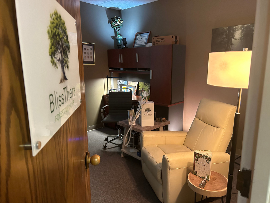 A door opens into the BlissThera treatment room with an armchair and a lamp.